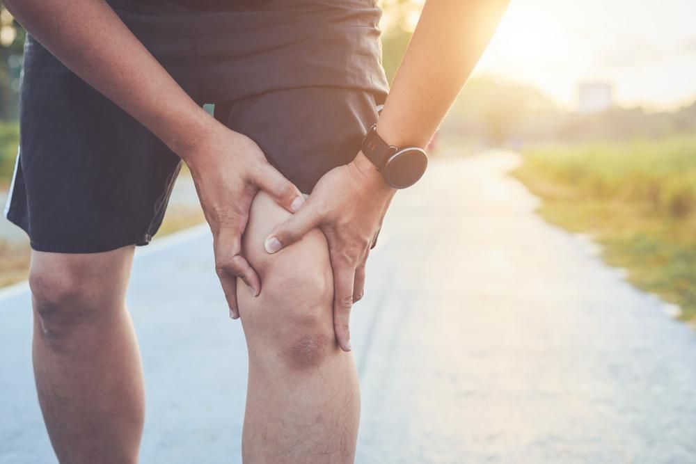 Person holding a knee on a sunlit path outdoors