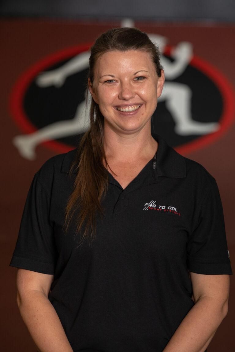 Smiling person in a black polo shirt standing before a red-and-black logo backdrop