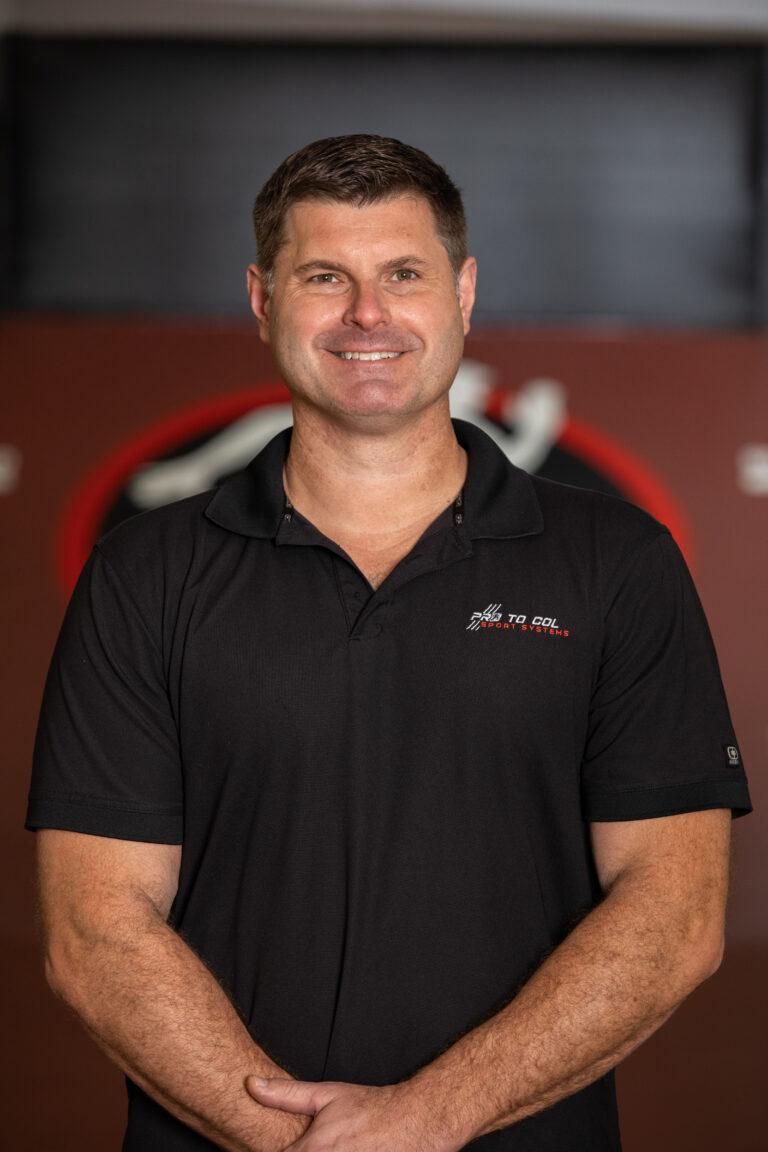 Smiling man in a black polo shirt standing indoors against a red and black background