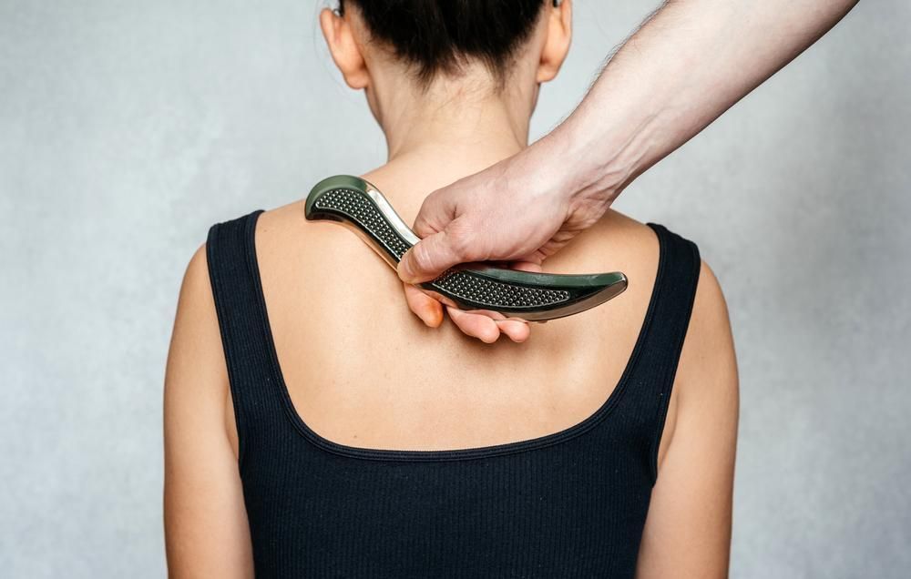 Hand using a green grooming brush on a person’s upper back and shoulders