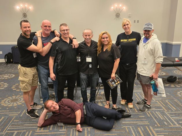 Group of people posing in a conference room; one person lies playfully on the floor in front.