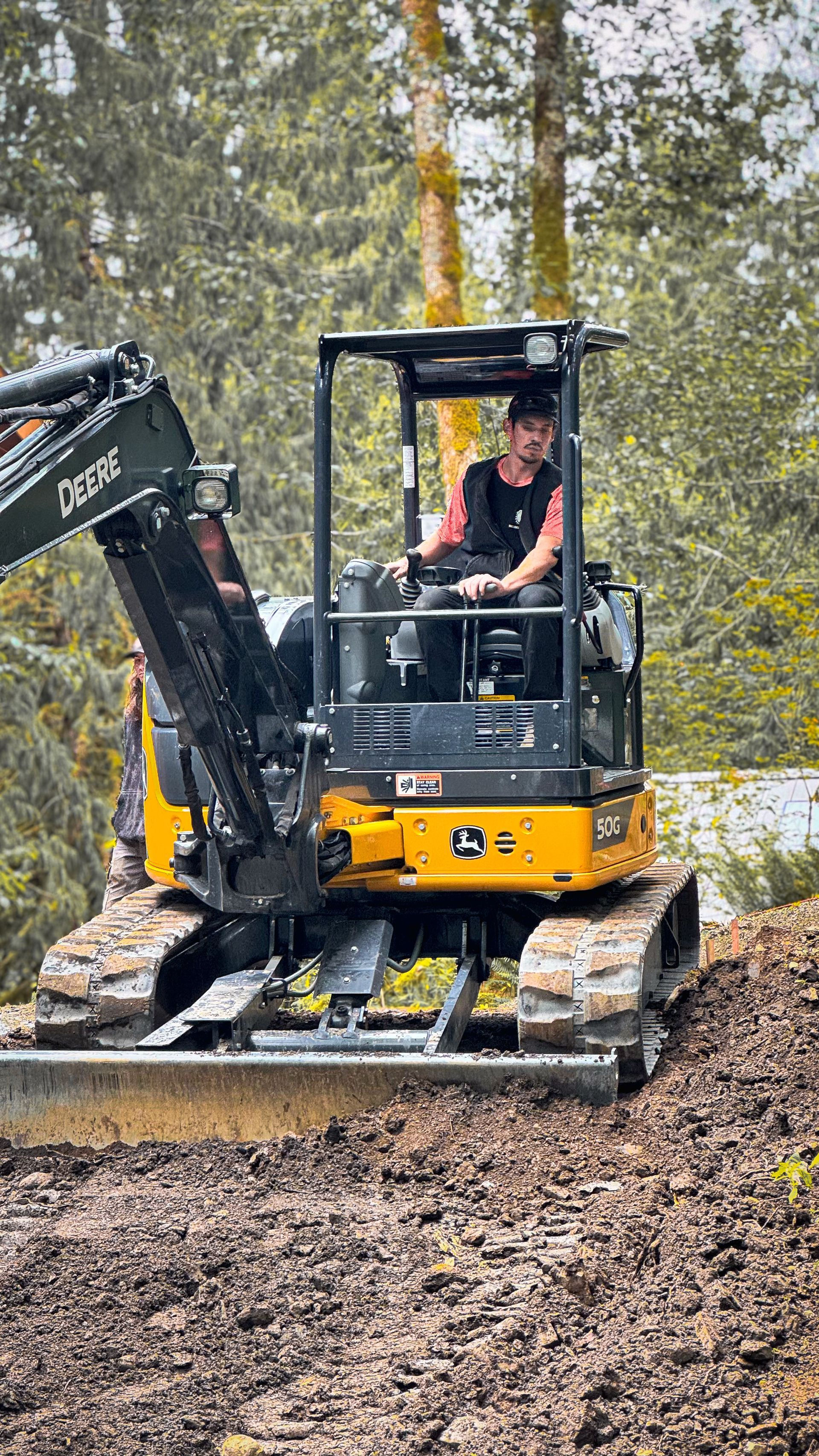 Person operating a yellow and black excavator in a wooded area.