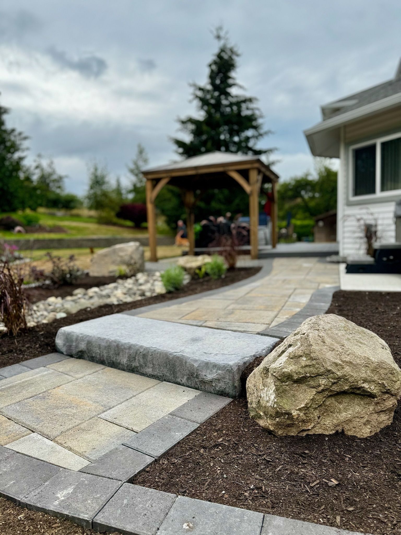 Stone walkway with rock border and gazebo in background.