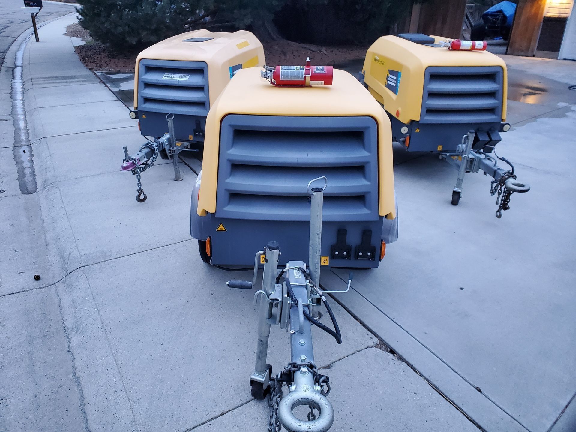Three yellow and gray industrial compressors on trailers parked on a paved surface.