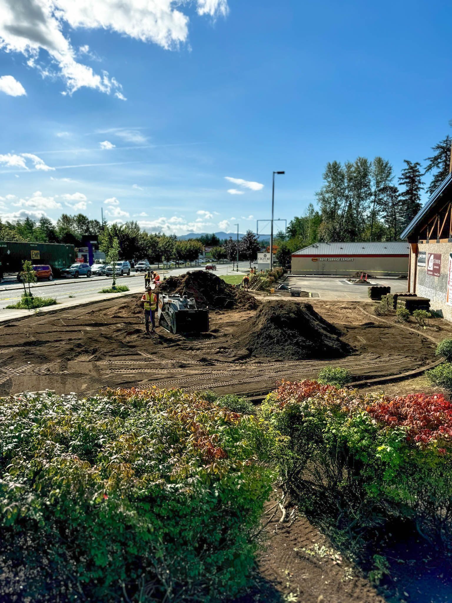 Construction site with dirt piles and workers under a blue sky near a building.