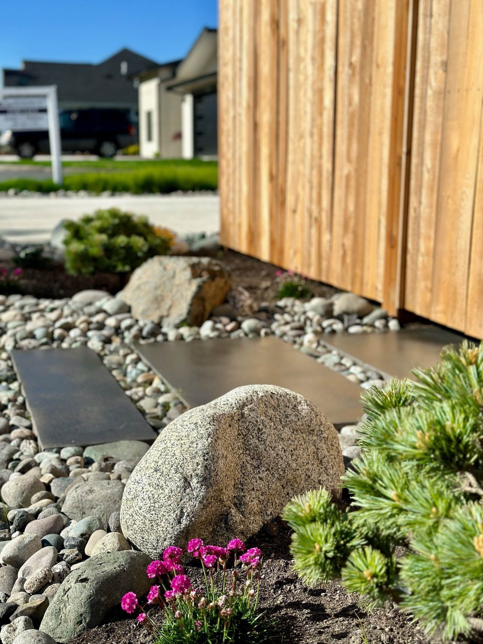 Stone pathway with river rocks and landscaping beside a wooden fence.