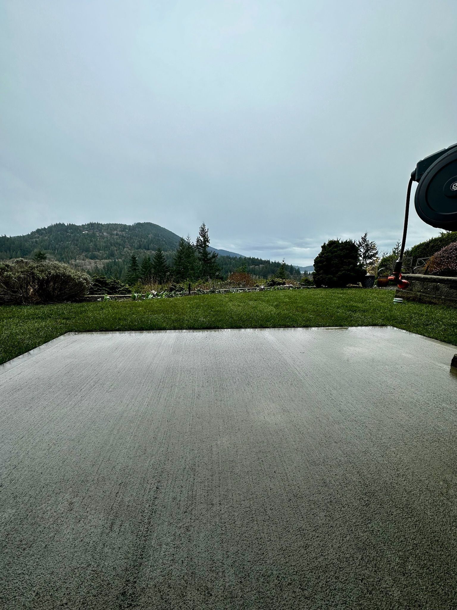 Wet patio and lawn with a distant green hill under an overcast sky.