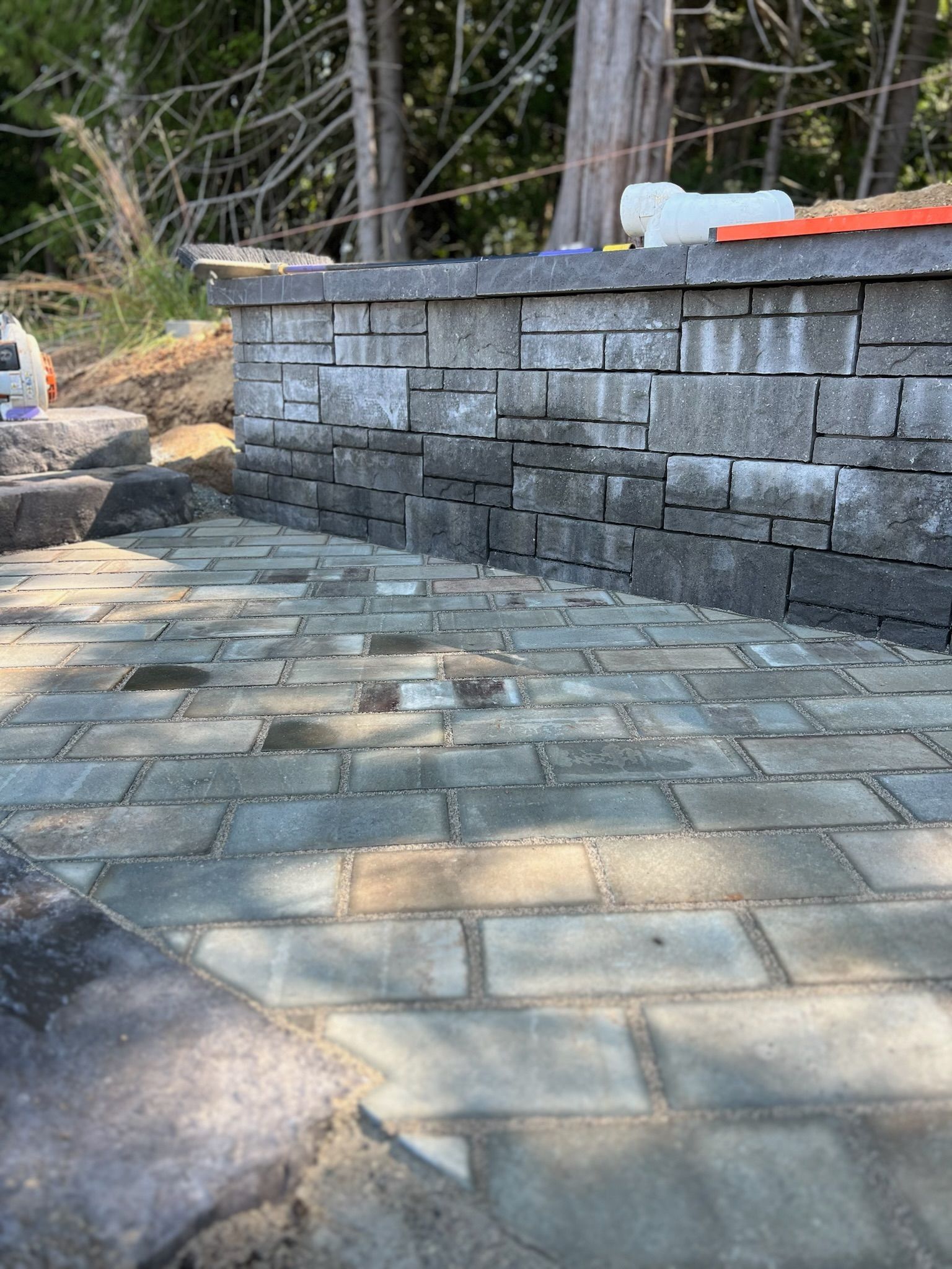 Stone patio and retaining wall, partially constructed with wet pavers and natural surroundings.