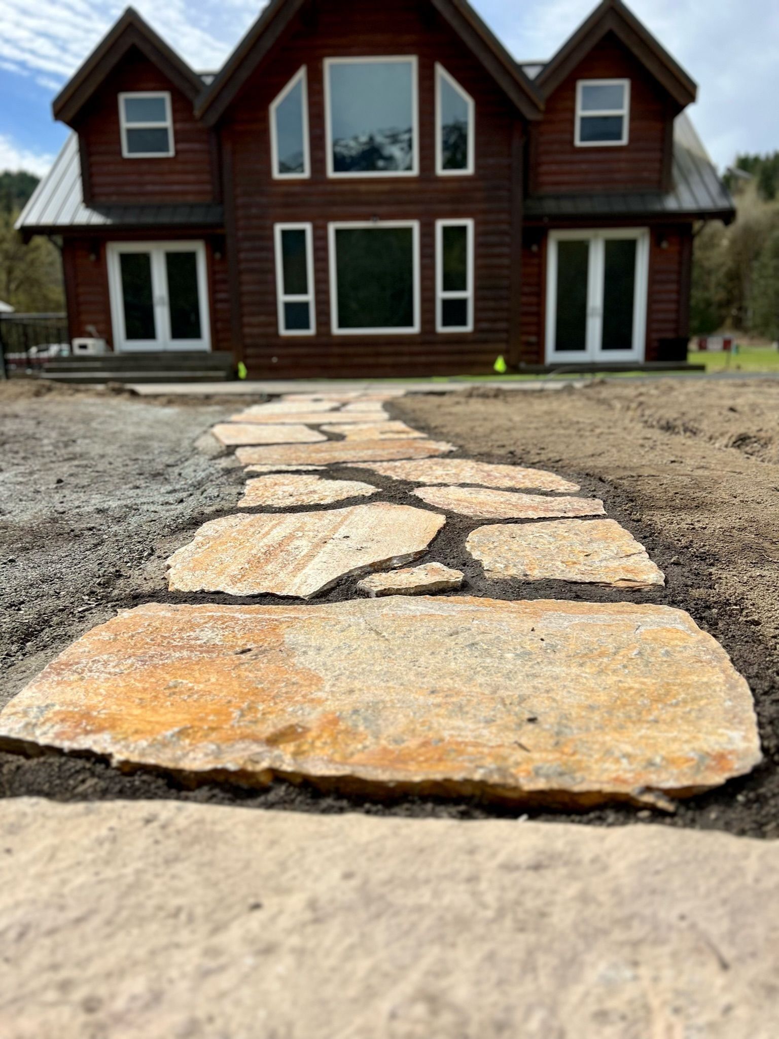 Stone path leading to a brown log cabin with large windows.