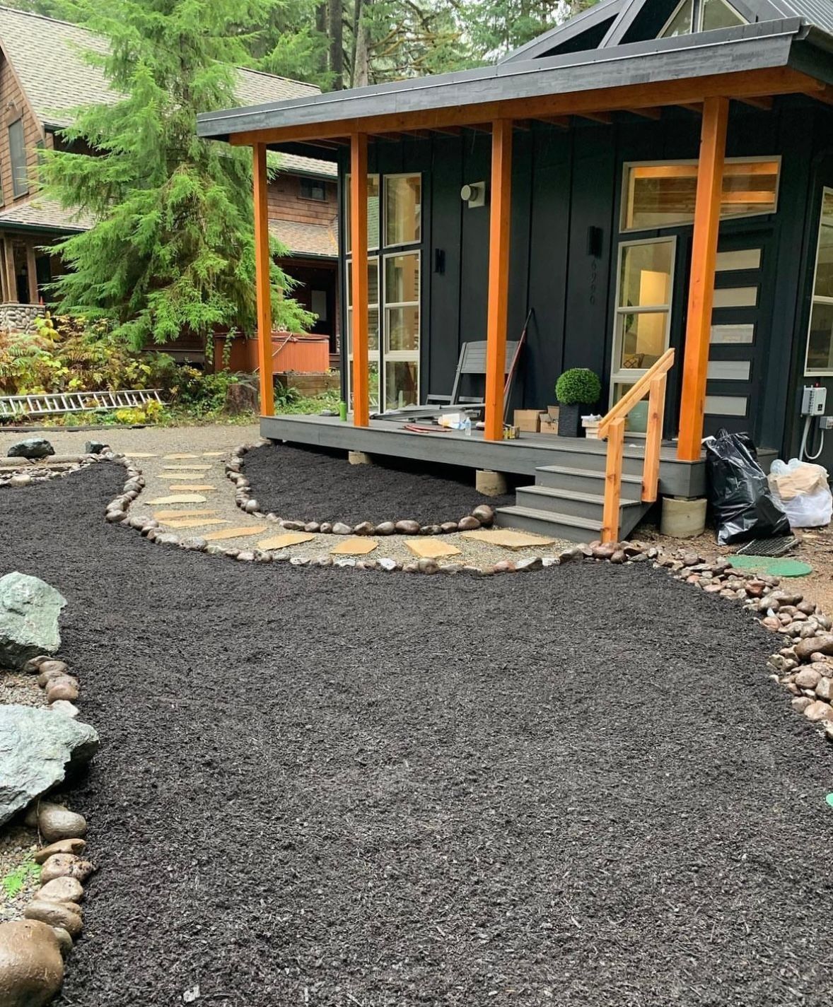 Small black house with a covered porch and gravel walkway.
