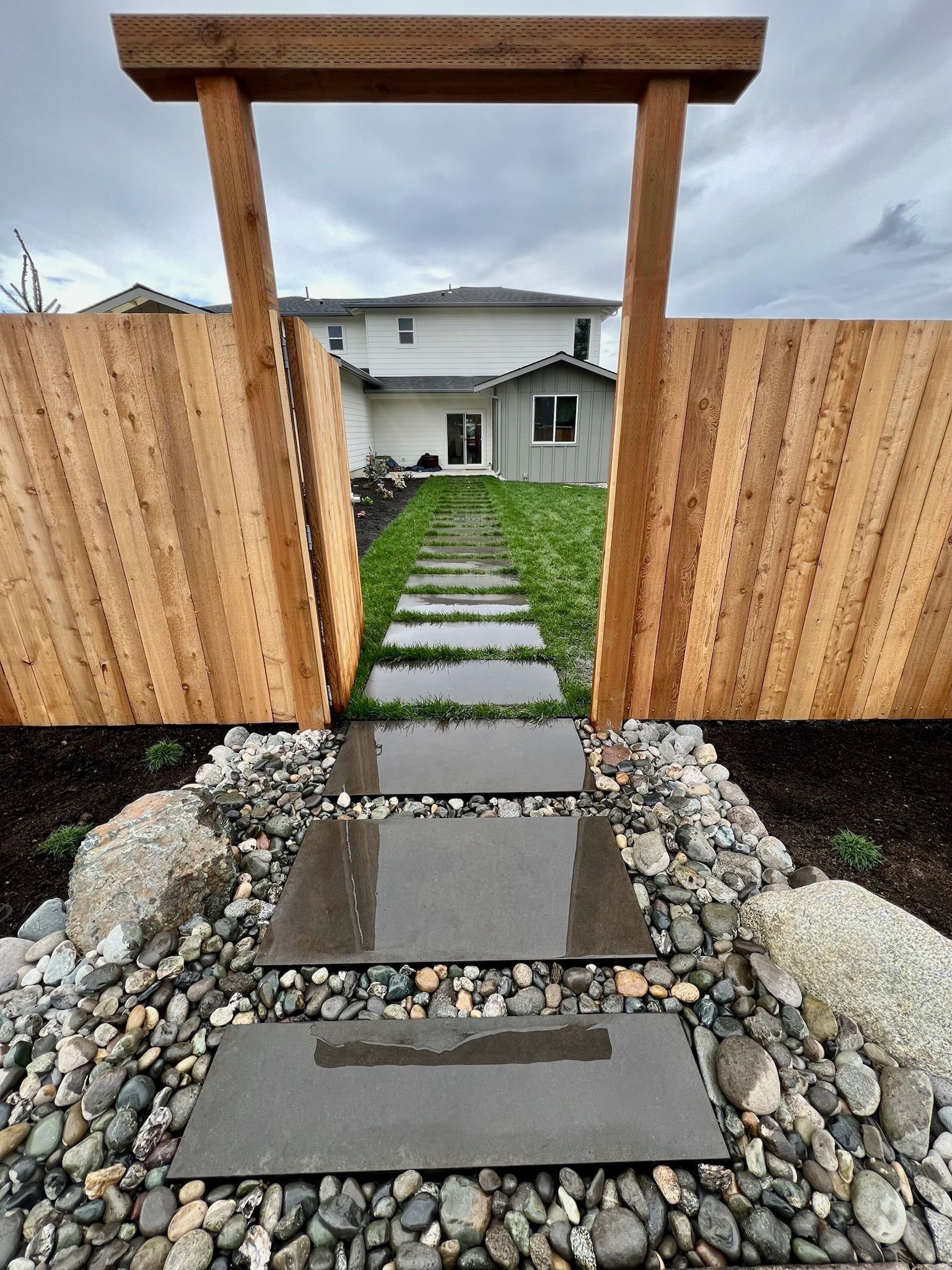 Wooden gate and fence frame a stepping stone path leading to a two-story house.
