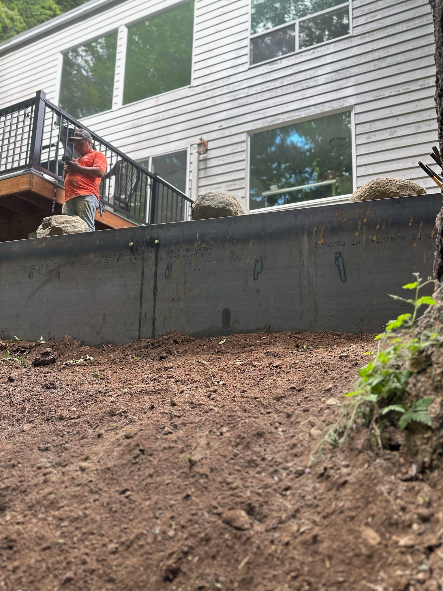 Person raking gravel near a concrete foundation of a two-story house with windows and a deck.