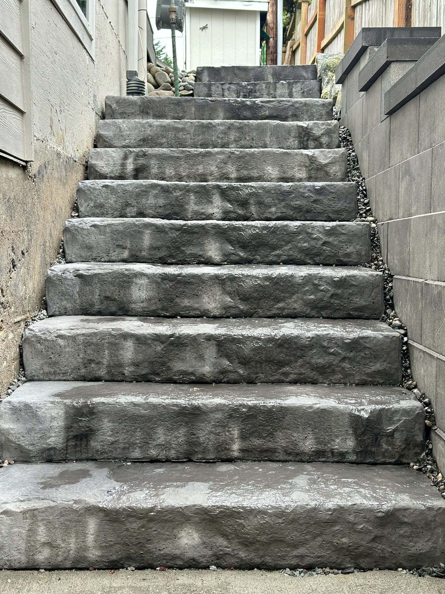 Stone staircase leading upwards, flanked by retaining walls. Gravel and buildings are visible.