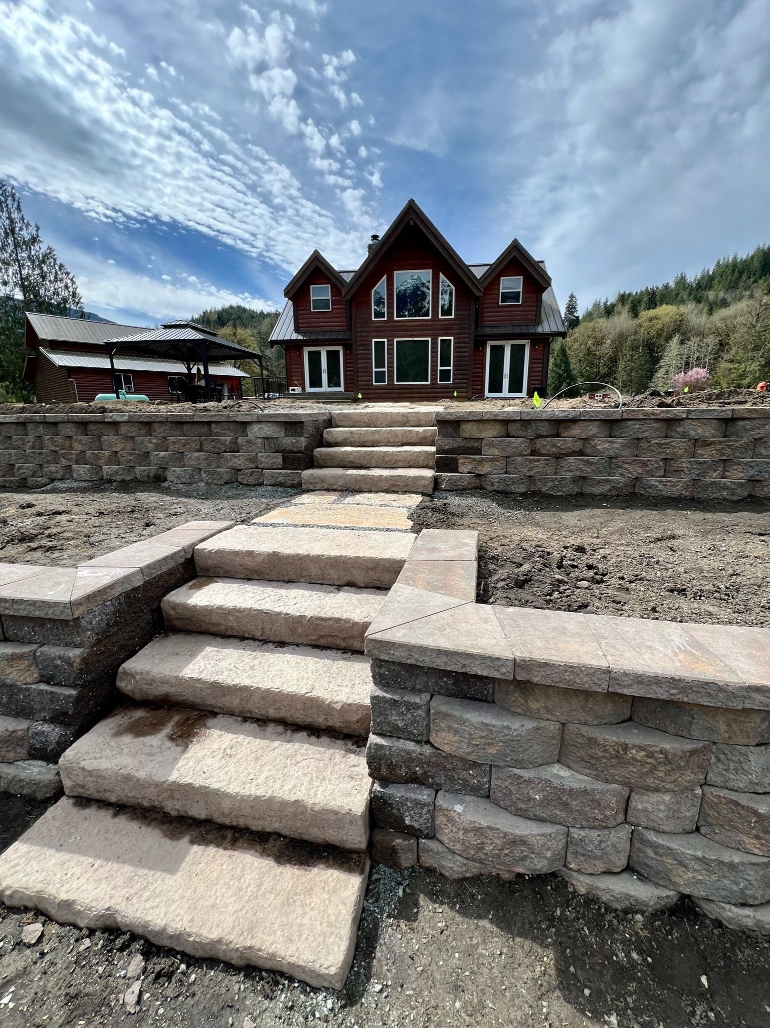 Stone steps leading up to a two-story brown house with large windows. Cloudy blue sky overhead.
