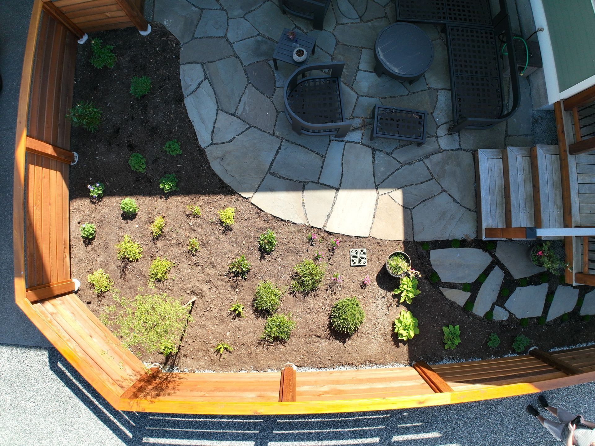 Overhead view of a backyard patio with stone pavers, wooden fence, and planted shrubs.