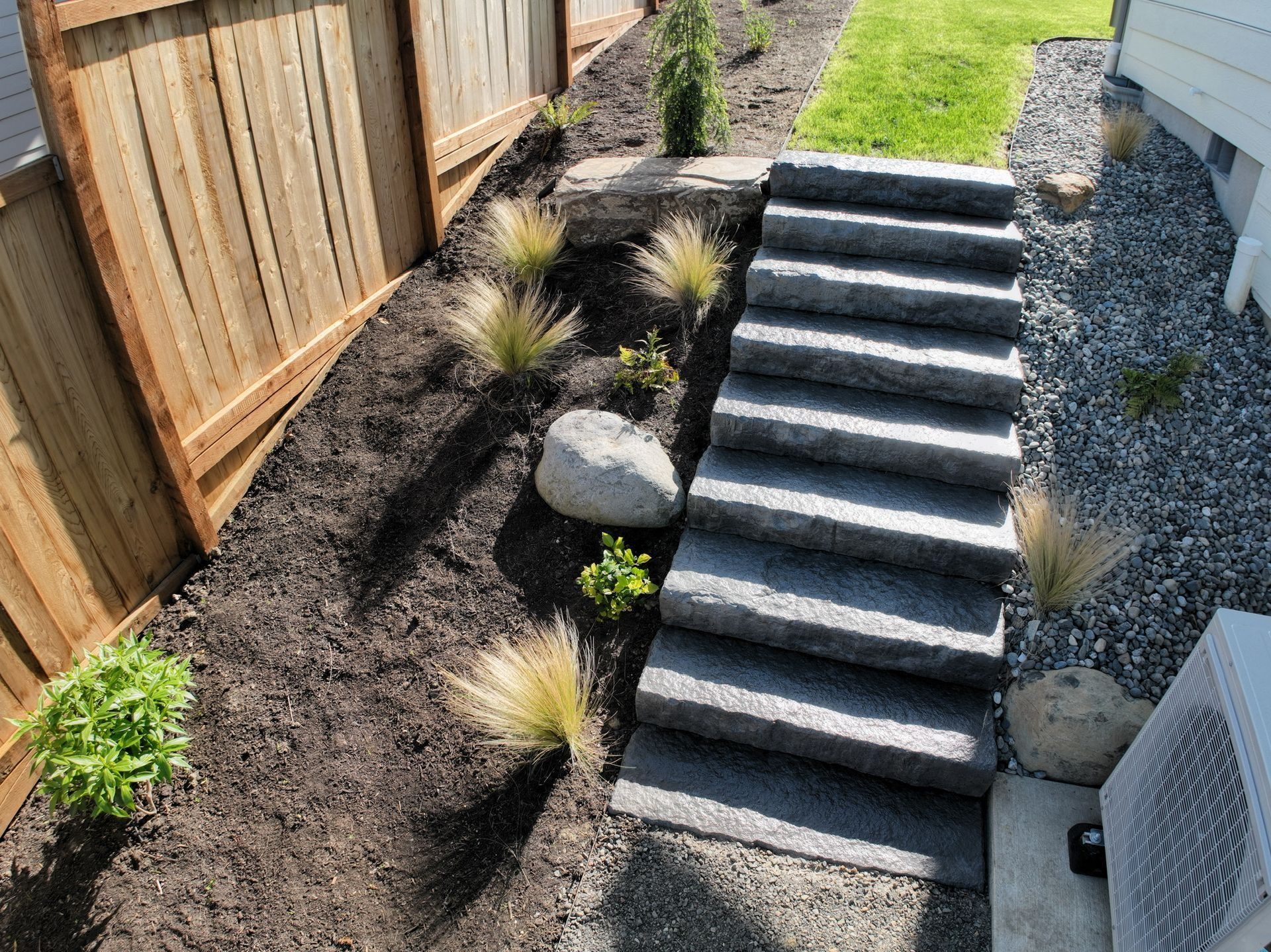Stone steps descend from a mulch and gravel landscaped yard with a wooden fence.