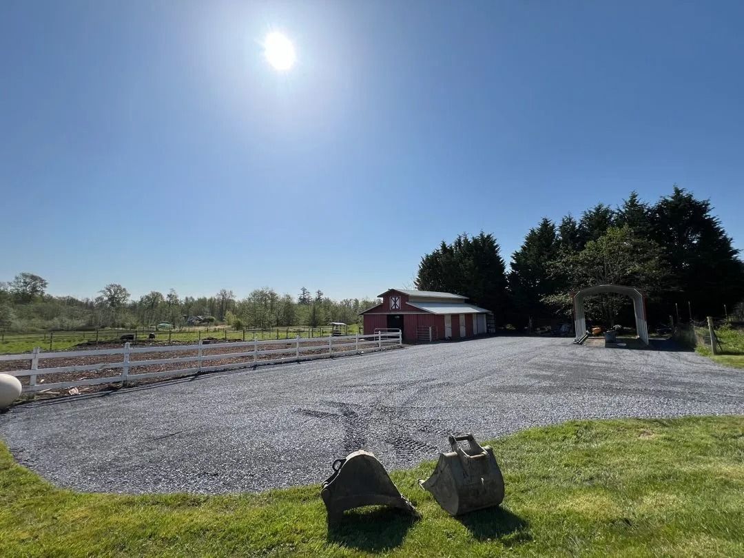 Red barn on gravel, white fence, trees, and sunny blue sky.