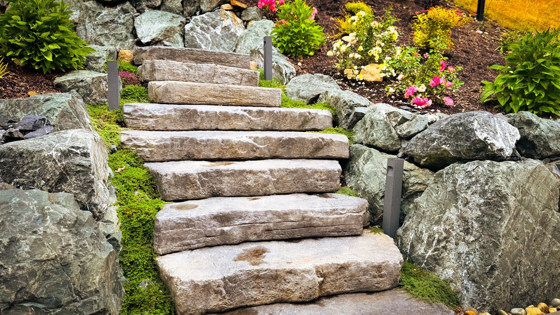 Stone steps lead up a rock-lined garden, with greenery and flowers