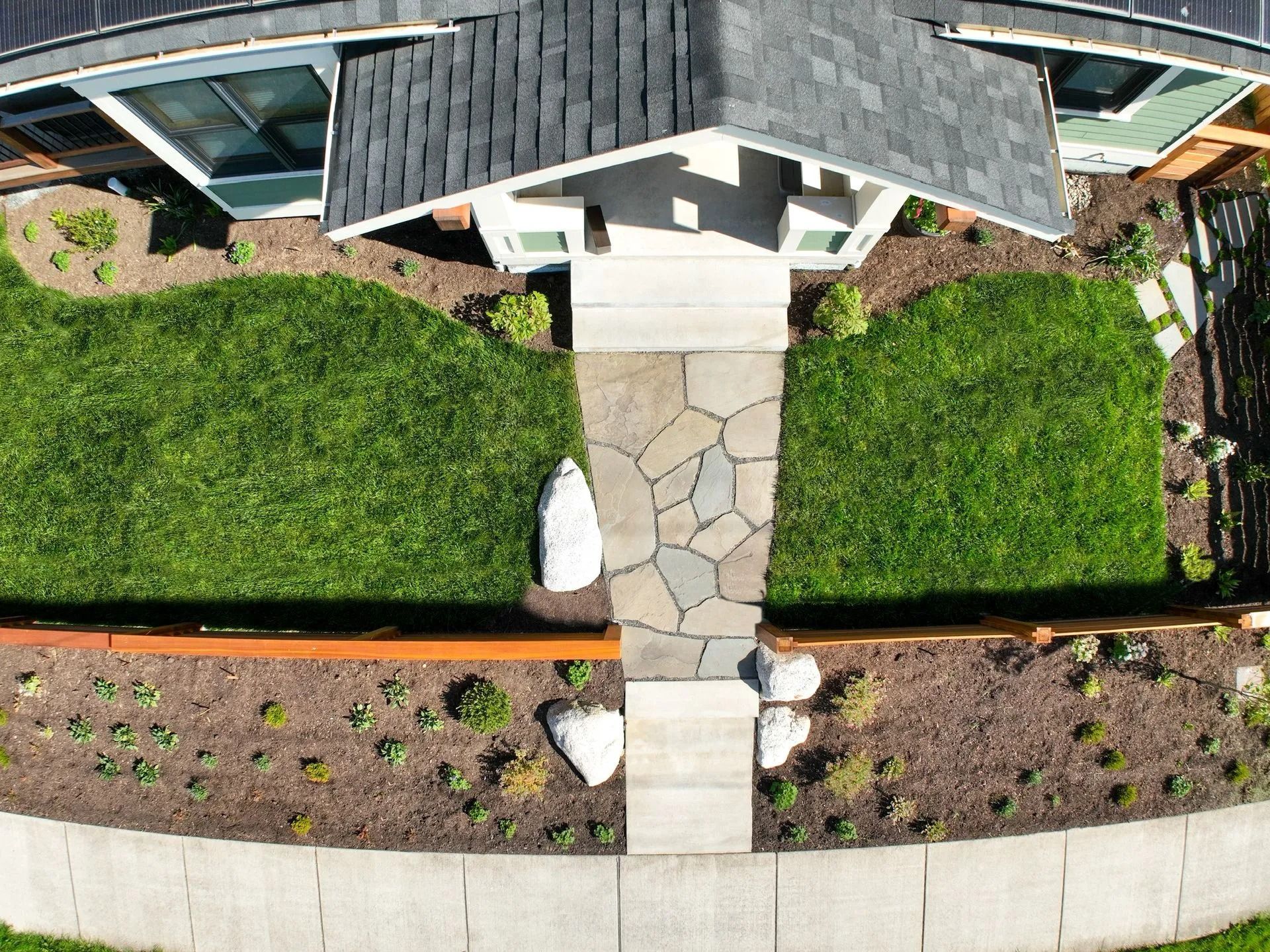 Overhead view of a house with a stone pathway leading to the front door, flanked by green grass and landscaping.