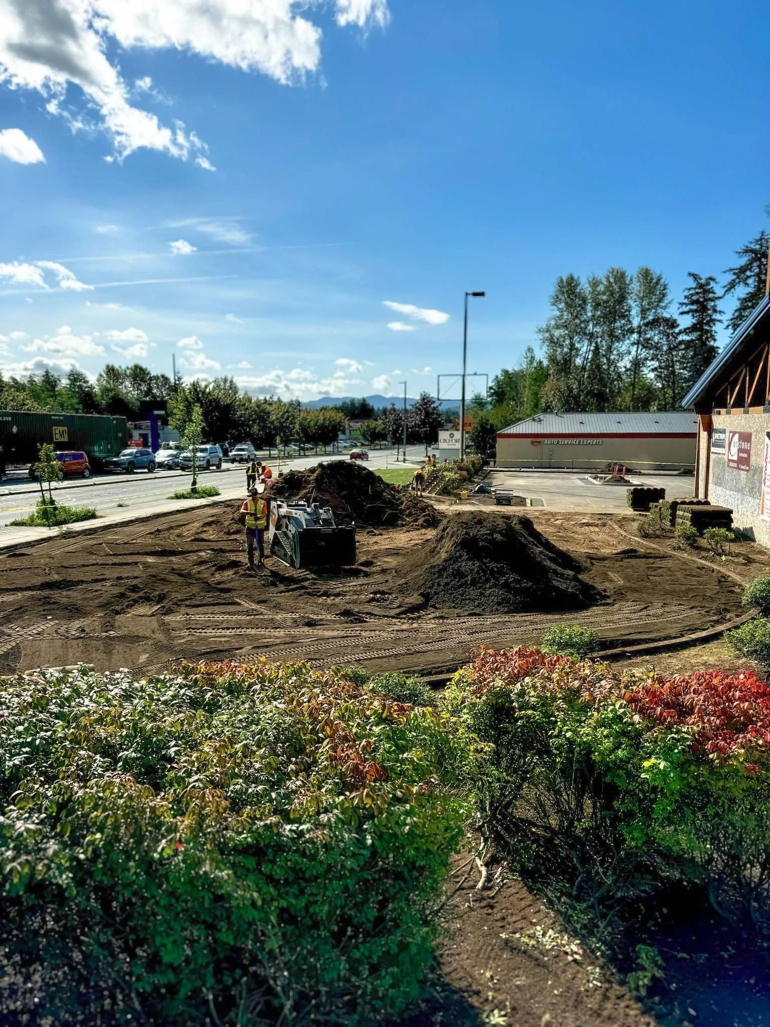 Construction site with piles of dirt, workers, and a building on a sunny day.