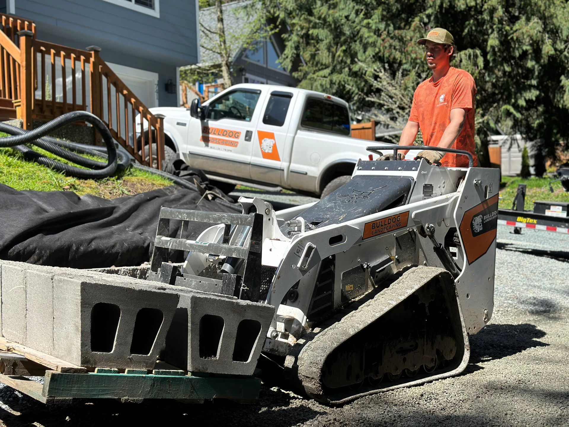 Construction worker beside a white pickup and a tracked machine on a gravel driveway