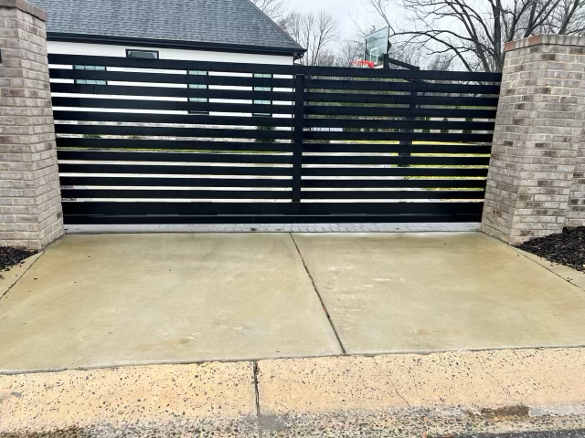 A black gate is sitting on top of a concrete driveway next to a brick wall.