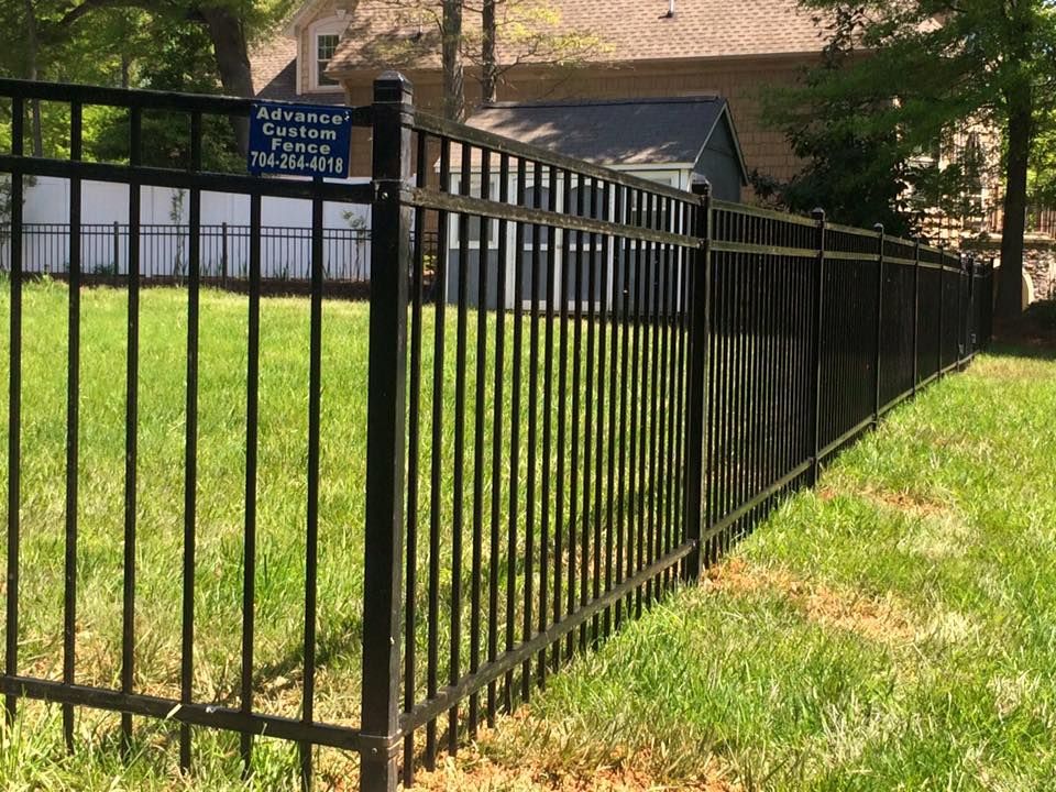 A black wrought iron fence surrounds a lush green field