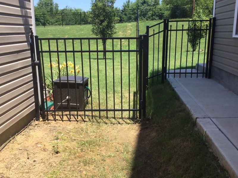 A black metal fence is surrounding a yard next to a house.