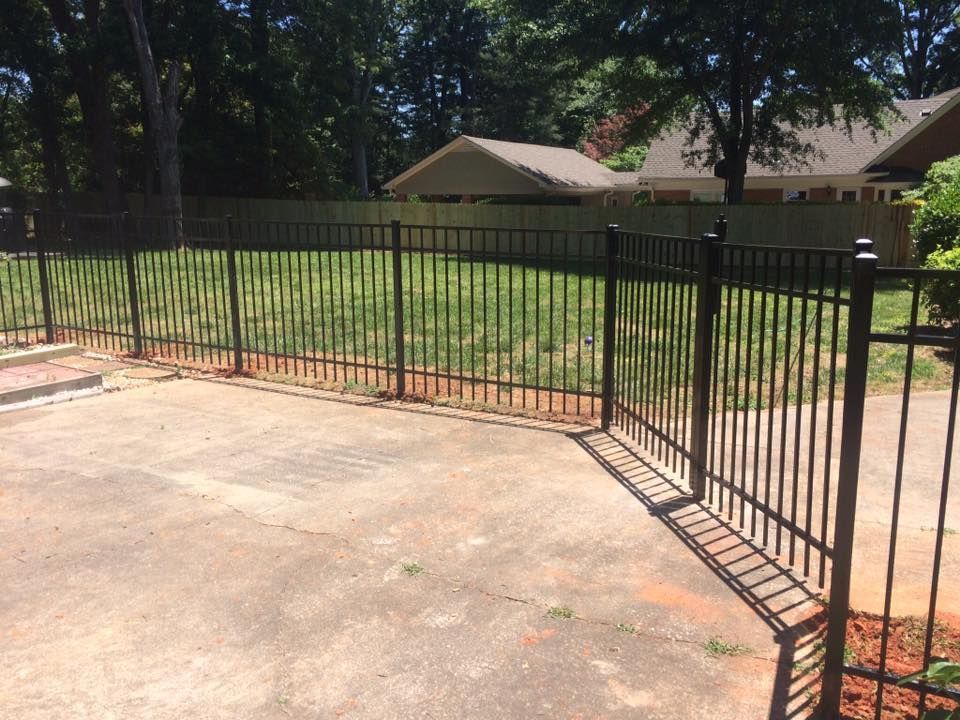 A black metal fence surrounds a driveway in front of a house