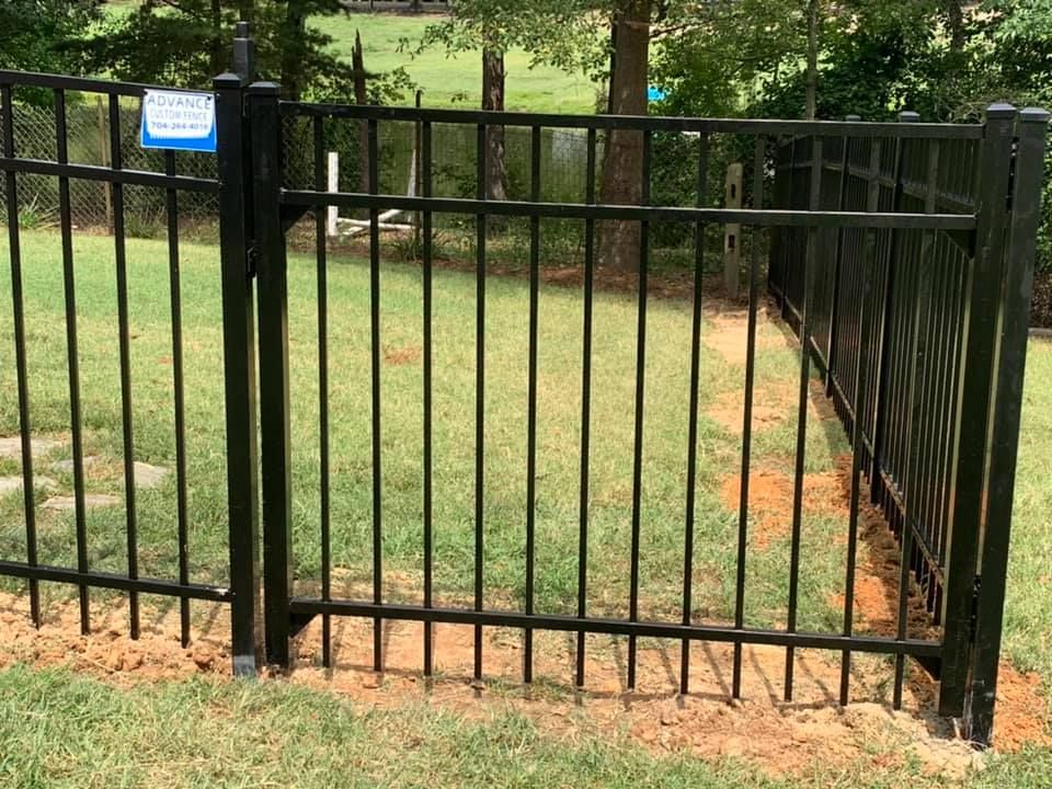 A black metal fence with a gate in the middle of a lush green field.