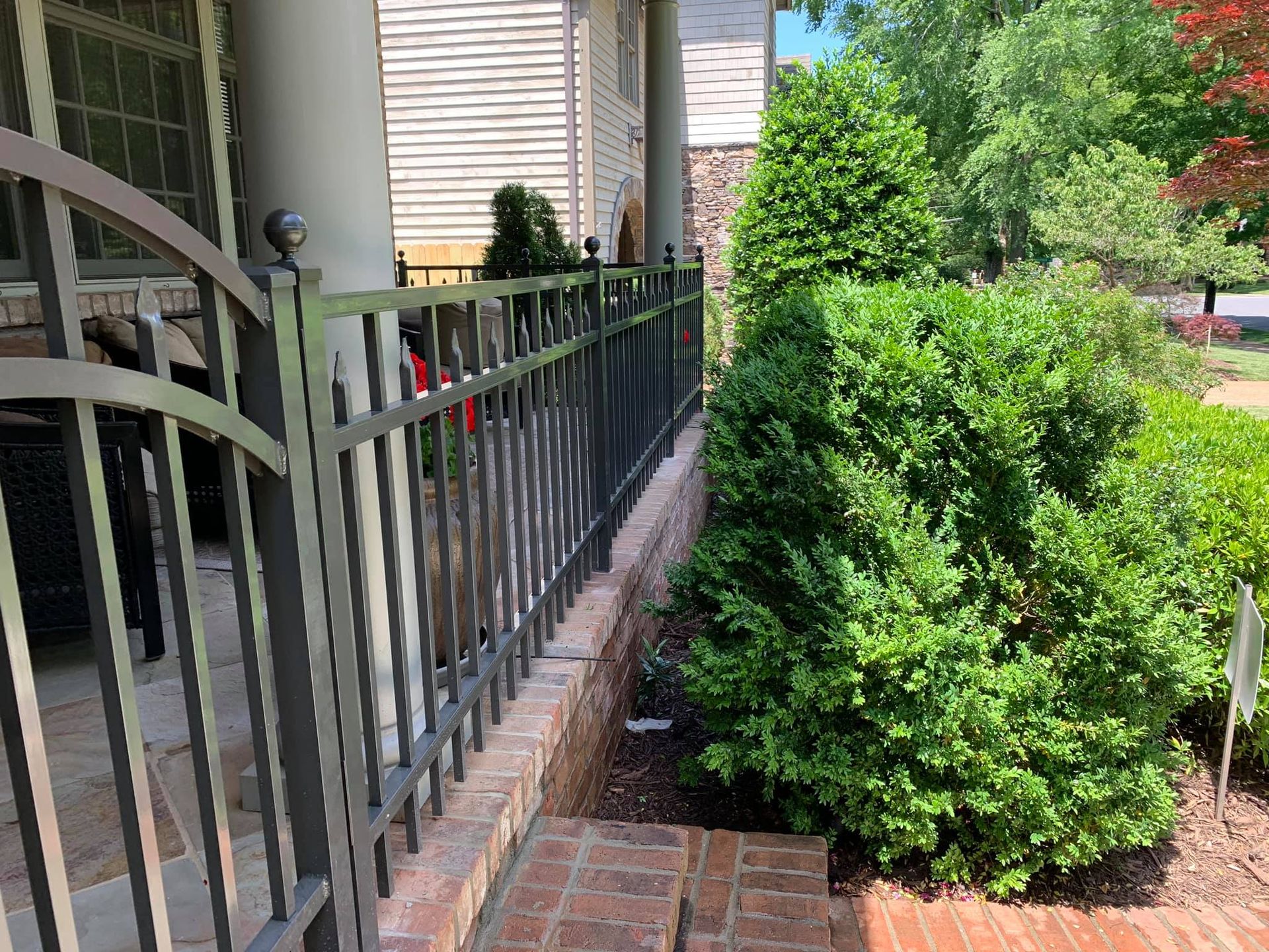 A metal fence surrounds a brick walkway in front of a house.