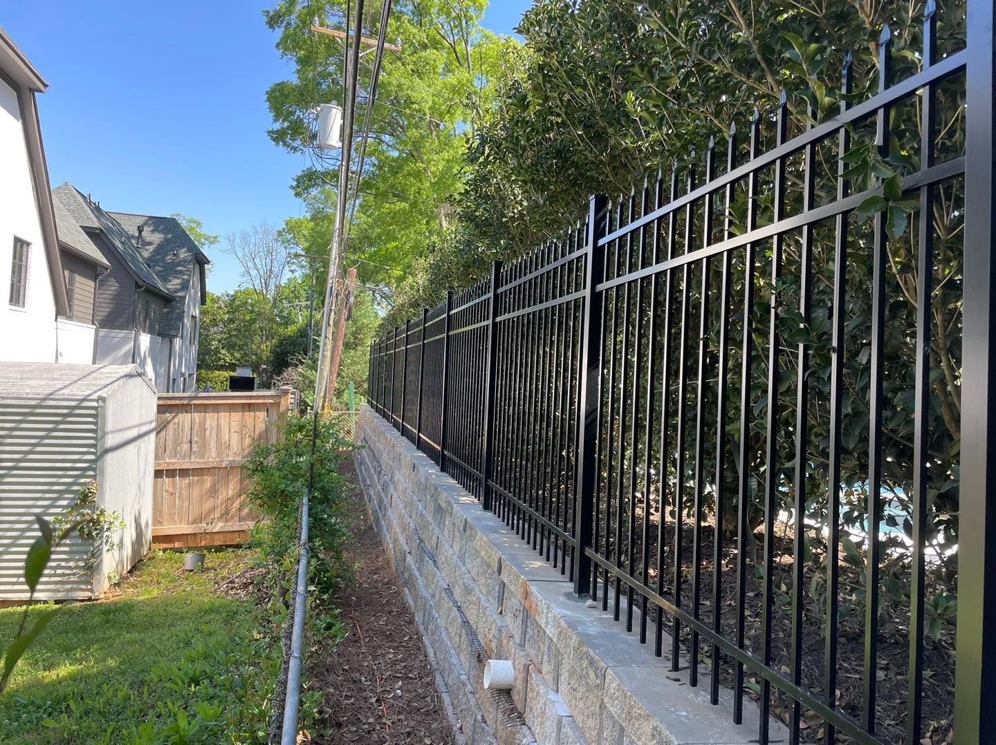 A black metal fence surrounds a stone wall in a backyard.