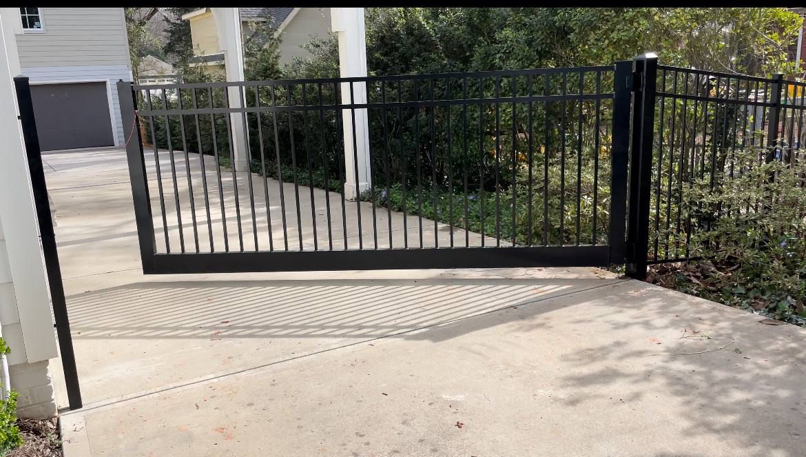 A black gate is open to a driveway in front of a house.