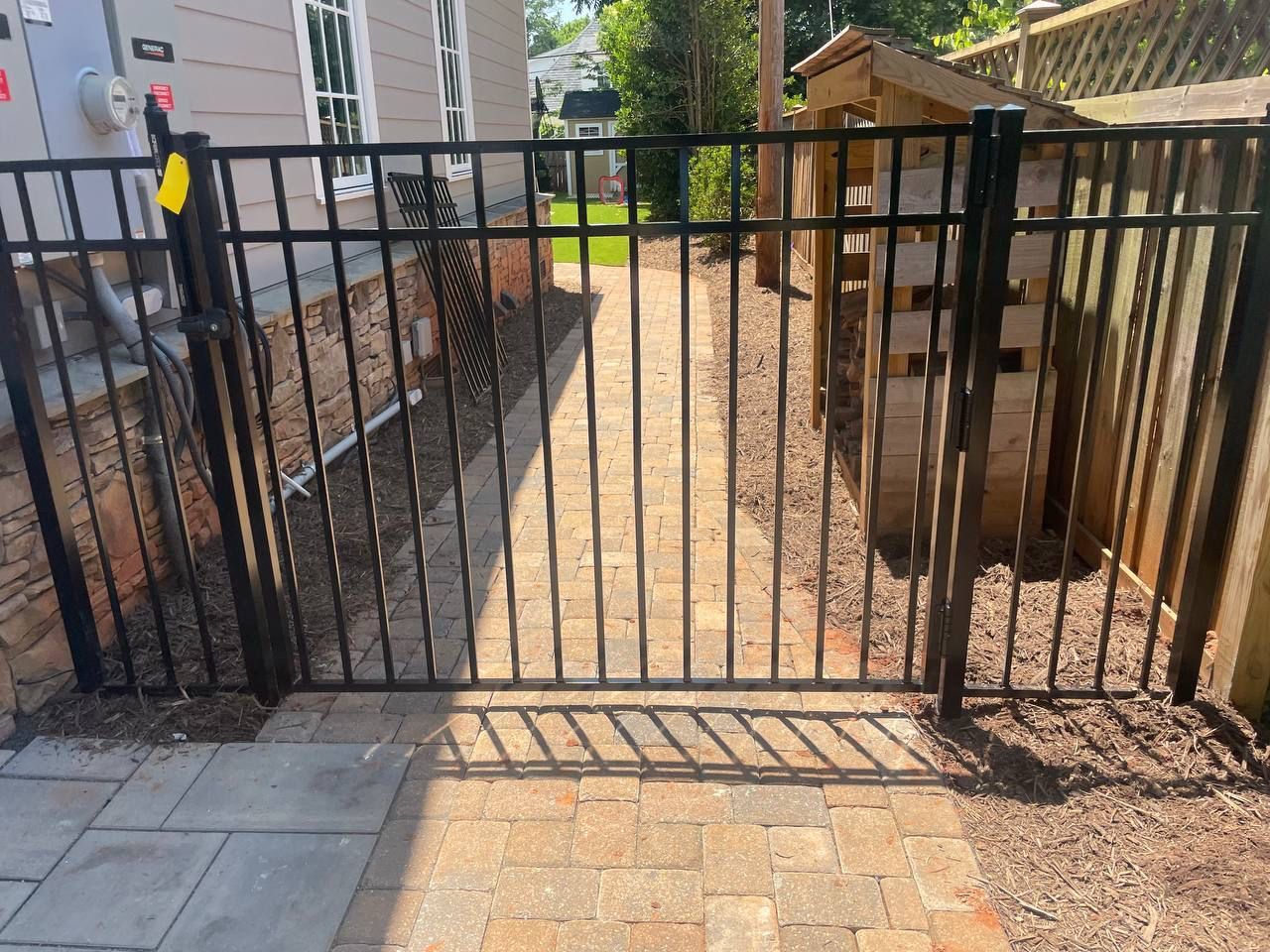 A black metal gate is open to a brick walkway leading to a house.