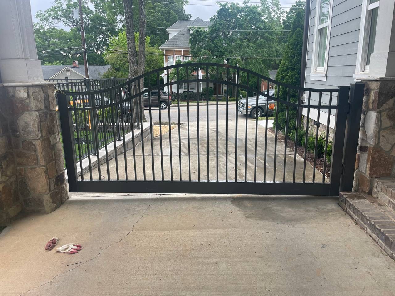 A black sliding gate is open to a driveway leading to a house.