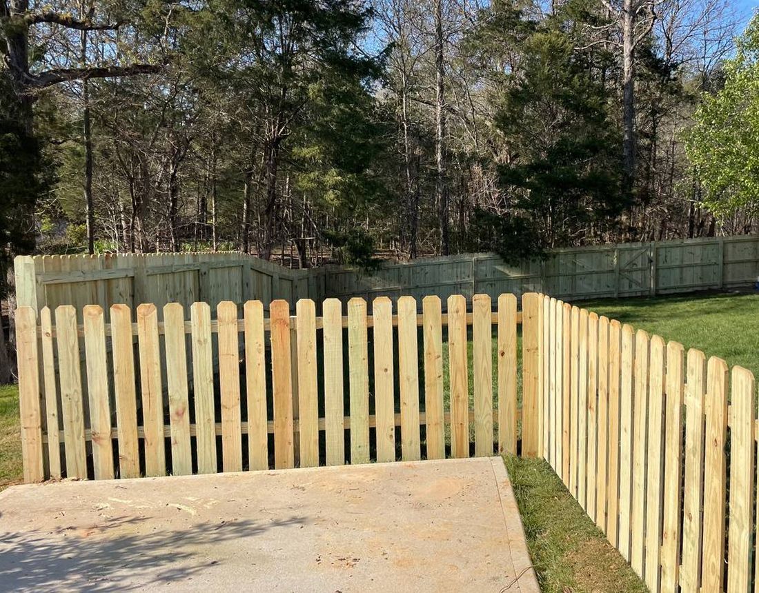A wooden picket fence surrounds a driveway in a yard.