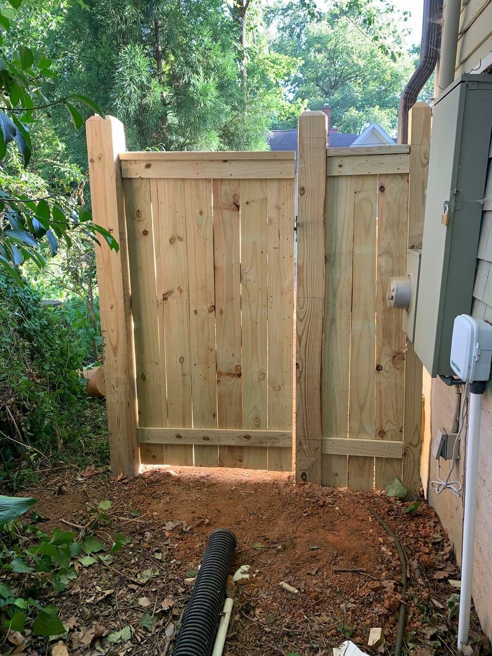 A wooden gate is sitting in the dirt next to a house.