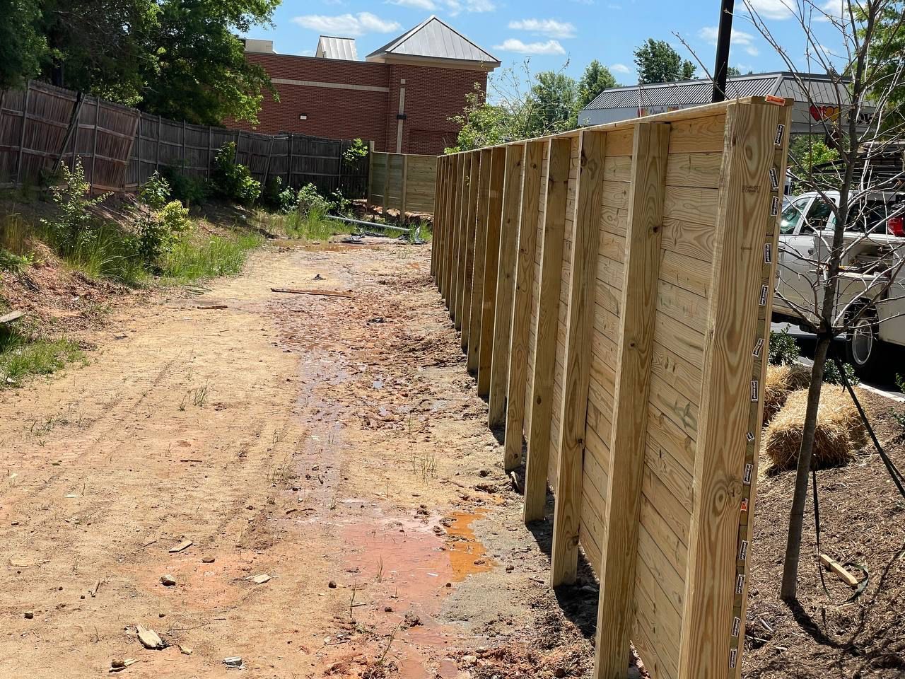 A wooden fence is sitting on the side of a dirt road.