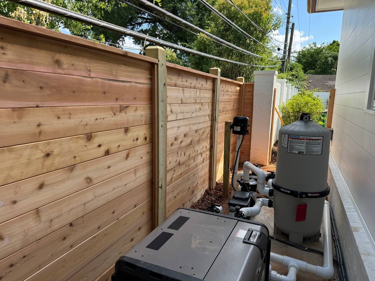 A wooden fence surrounds a pool with a vacuum cleaner.