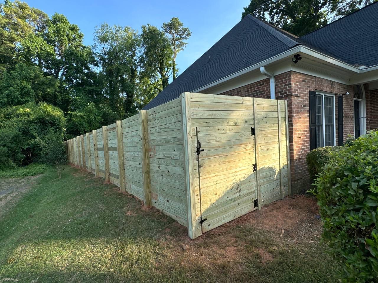 A wooden fence is in front of a brick house.