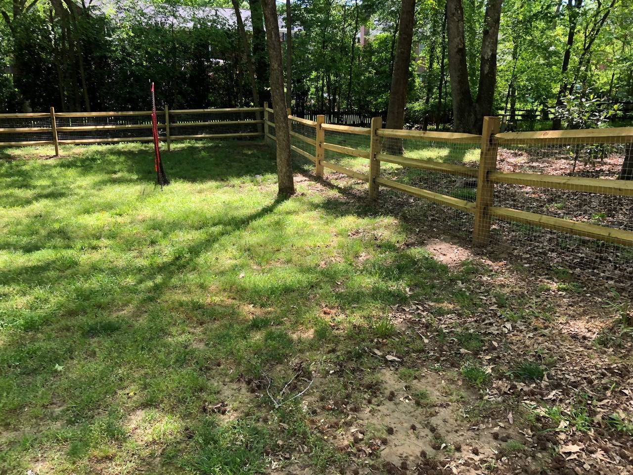 A wooden fence surrounds a lush green field.