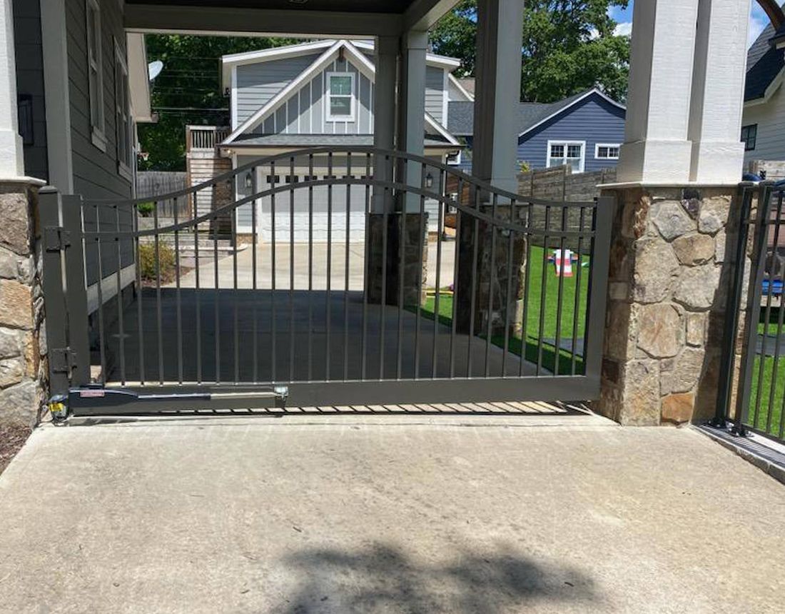 A metal gate is open to a driveway in front of a house.