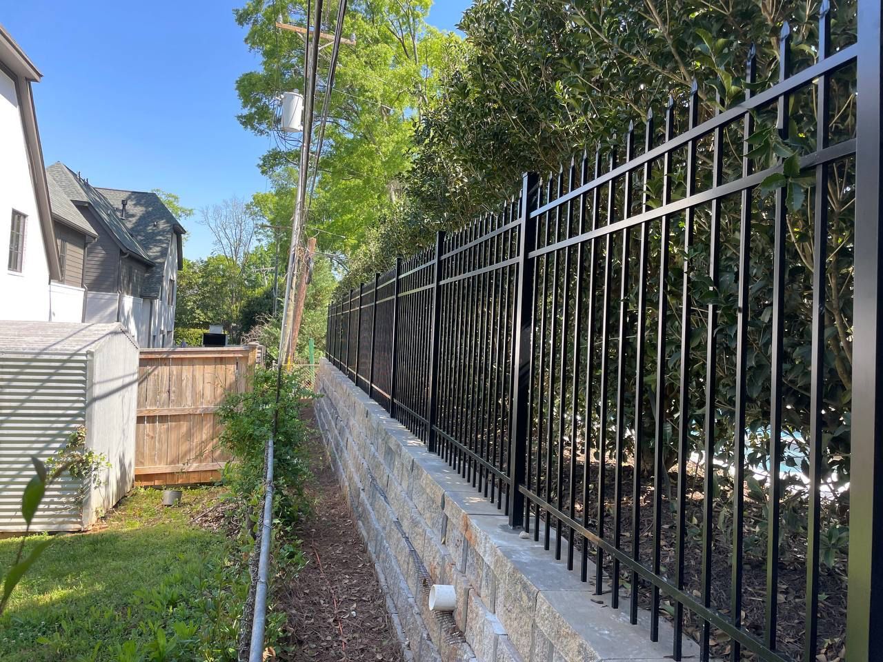 A black metal fence surrounds a stone wall in a backyard.