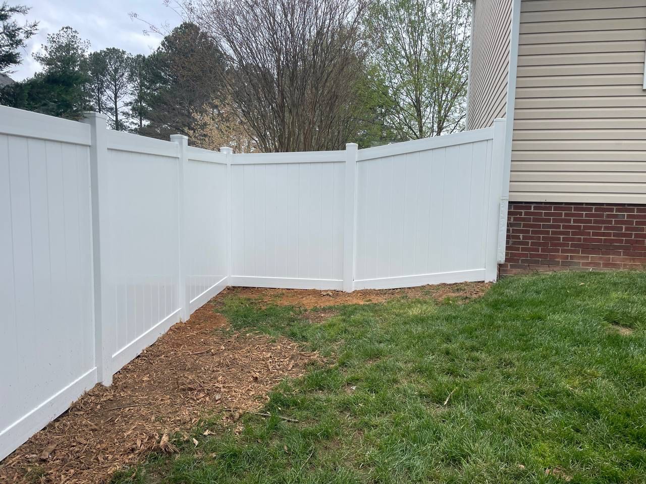 A white vinyl fence is in the backyard of a house.