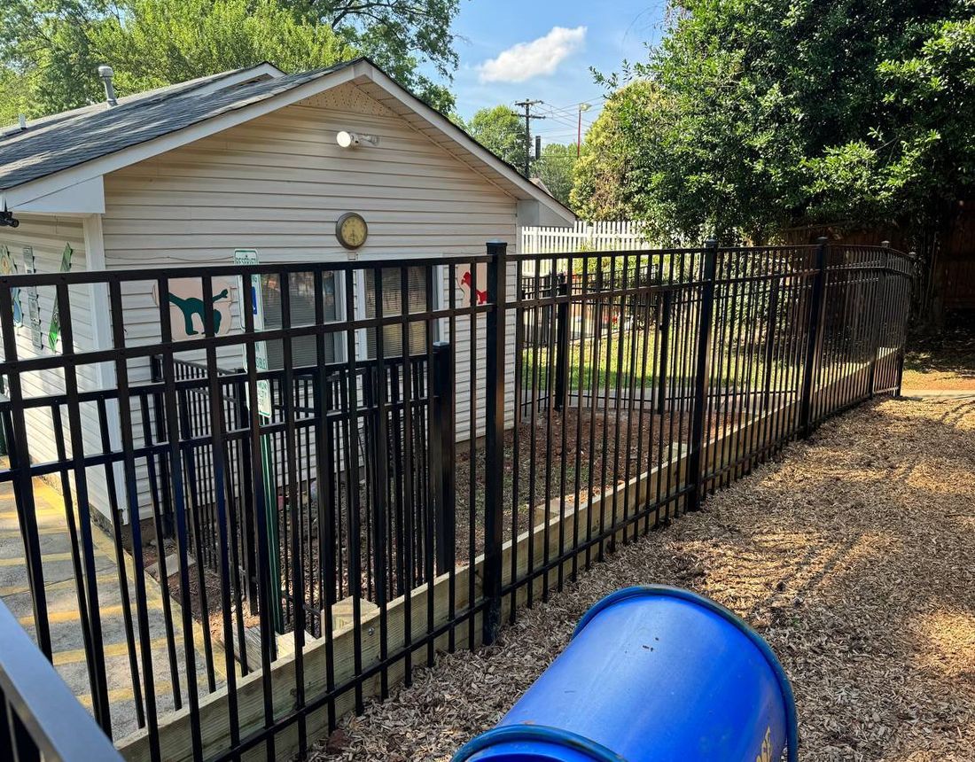 A black fence surrounds a playground in front of a house.