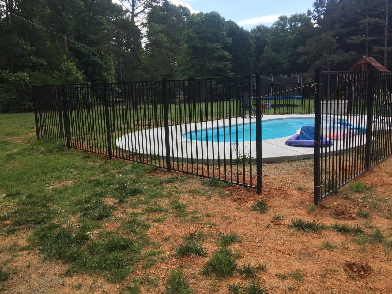 A fence surrounds a swimming pool in a backyard.