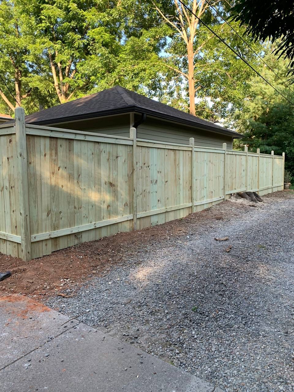 A wooden fence is sitting on the side of a gravel road next to a house.