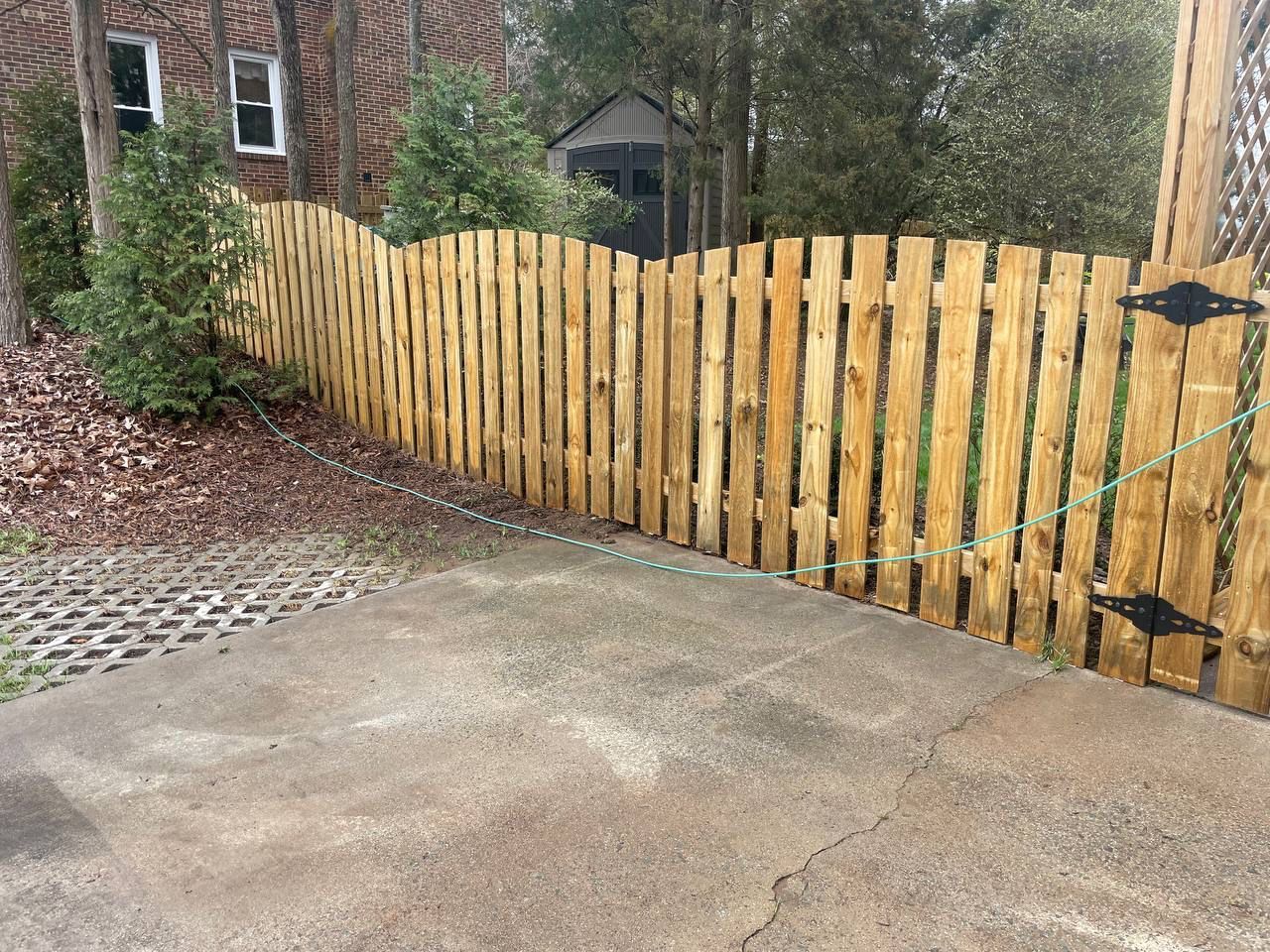 A wooden fence is surrounding a concrete driveway in front of a house.