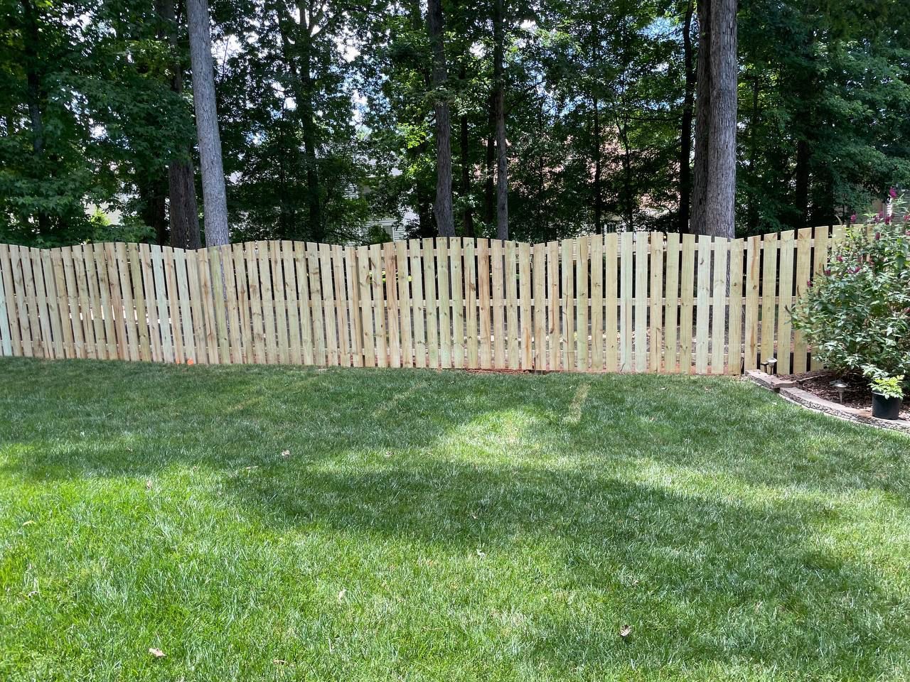 A wooden fence surrounds a lush green lawn in a backyard.
