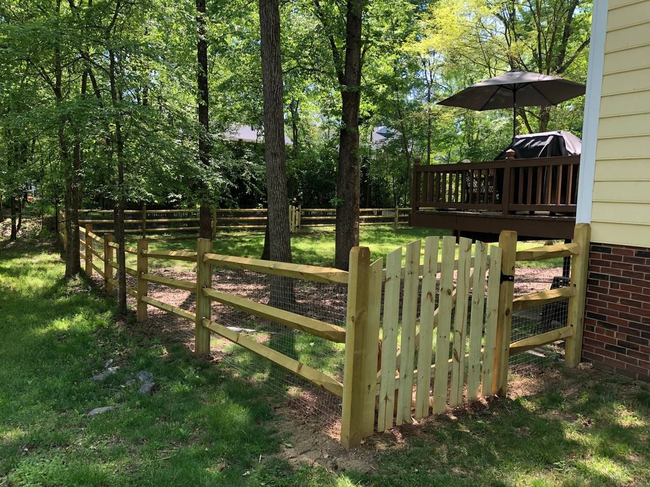 A wooden fence surrounds a backyard with a deck and umbrella.